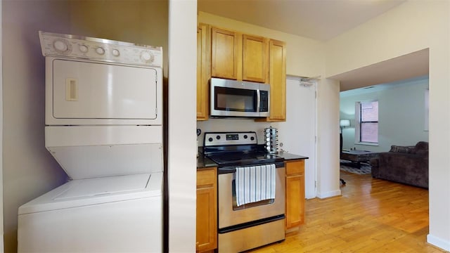 kitchen featuring light wood-type flooring, stainless steel appliances, dark countertops, and stacked washer / drying machine