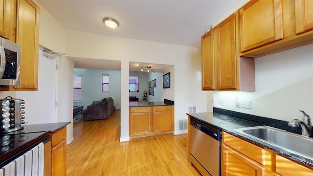 kitchen with dark countertops, light wood finished floors, appliances with stainless steel finishes, and a sink