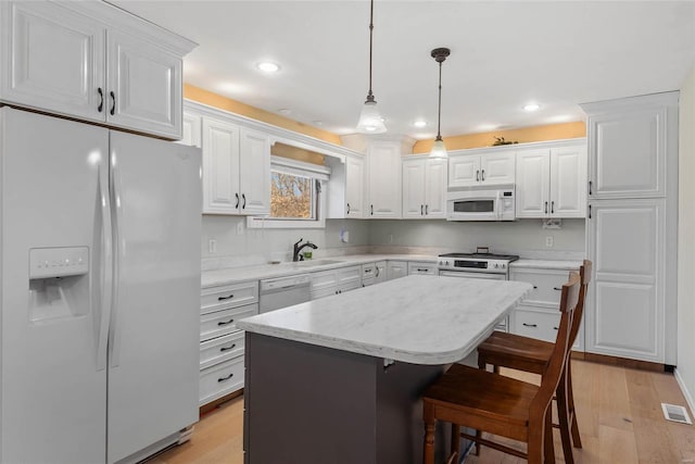 kitchen with a kitchen bar, white appliances, white cabinets, and light wood-style flooring