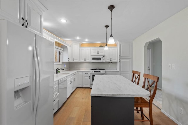 kitchen featuring a breakfast bar area, arched walkways, white cabinets, white appliances, and a sink