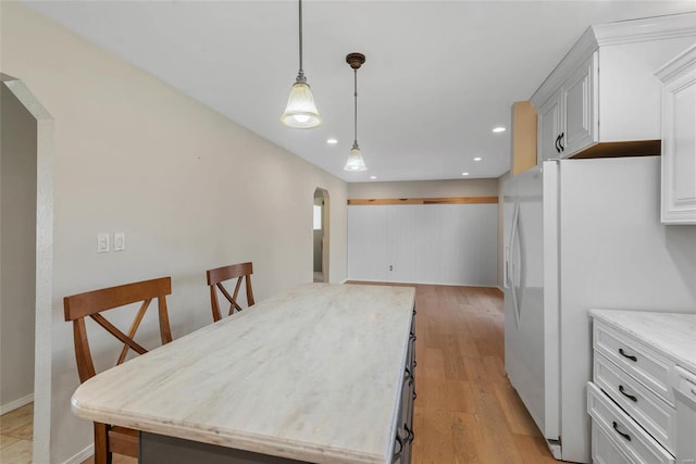 kitchen featuring a kitchen island, hanging light fixtures, light wood-style flooring, freestanding refrigerator, and arched walkways