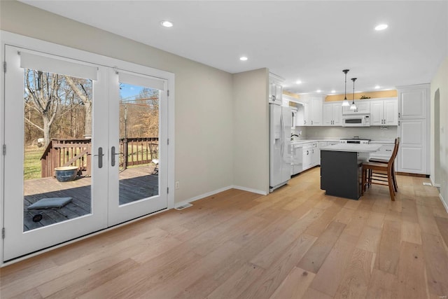 kitchen featuring white appliances, light wood finished floors, a breakfast bar, light countertops, and white cabinets