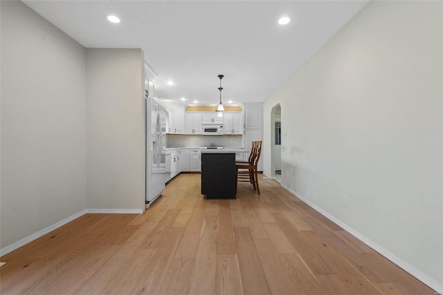 unfurnished dining area featuring recessed lighting, baseboards, arched walkways, and light wood finished floors