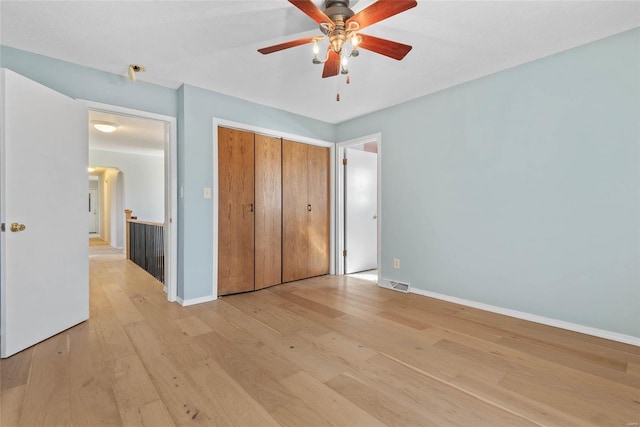 unfurnished bedroom featuring visible vents, ceiling fan, baseboards, light wood-style floors, and a closet