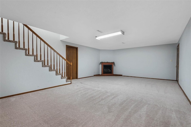 unfurnished living room with stairway, a fireplace with raised hearth, carpet, and baseboards