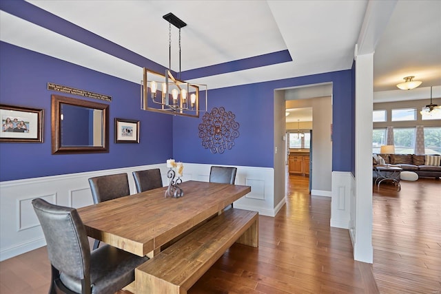 dining room featuring wainscoting, an inviting chandelier, a tray ceiling, and wood finished floors