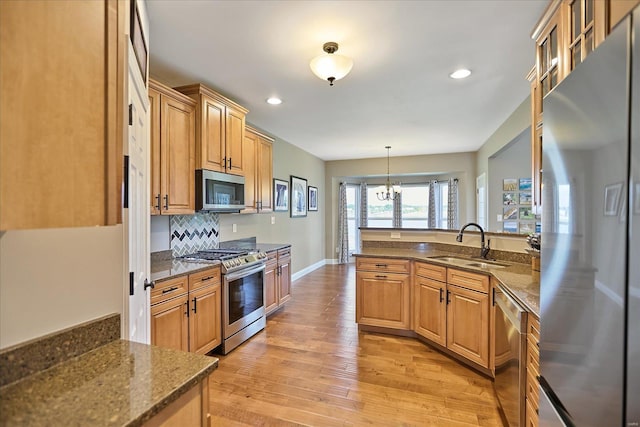 kitchen featuring light wood finished floors, tasteful backsplash, baseboards, appliances with stainless steel finishes, and a sink