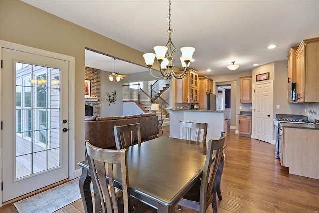 dining area featuring stairway, wood finished floors, recessed lighting, a fireplace, and ceiling fan with notable chandelier