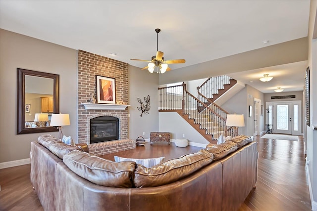 living room featuring stairway, baseboards, a brick fireplace, and wood finished floors