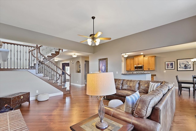 living room with light wood-style flooring, a ceiling fan, arched walkways, baseboards, and stairs