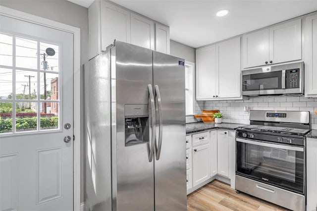 kitchen with backsplash, white cabinetry, stainless steel appliances, and light wood-style floors