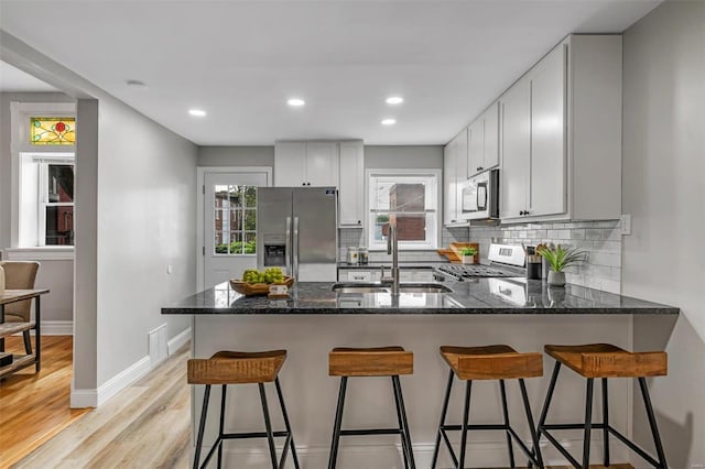 kitchen with tasteful backsplash, dark stone countertops, appliances with stainless steel finishes, a peninsula, and a sink