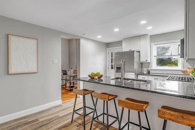 kitchen with stainless steel refrigerator with ice dispenser, dark stone counters, a peninsula, a breakfast bar area, and decorative backsplash