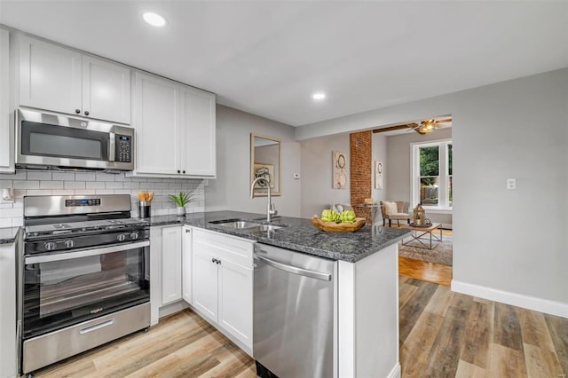 kitchen with light wood finished floors, decorative backsplash, appliances with stainless steel finishes, a peninsula, and a sink