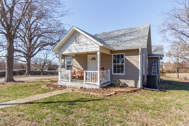 bungalow with cooling unit, a porch, a shingled roof, and a front lawn