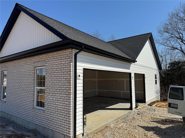 view of property exterior with an attached garage, brick siding, and roof with shingles