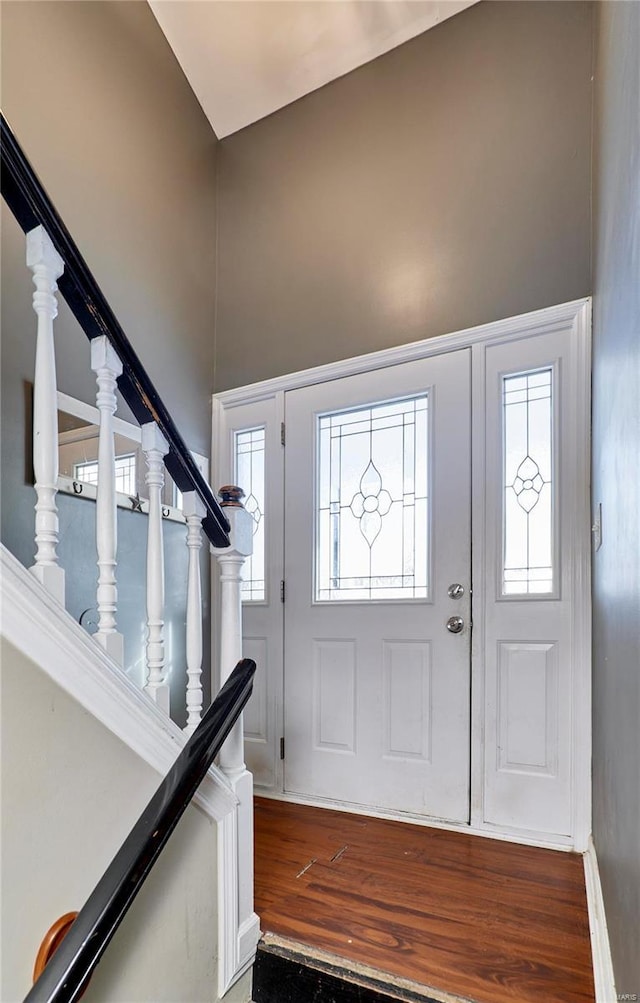 entrance foyer with stairs, a towering ceiling, and wood finished floors