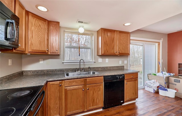 kitchen with visible vents, dark wood finished floors, a sink, black appliances, and dark countertops