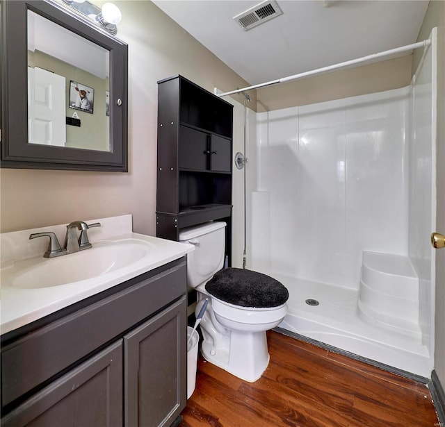 bathroom featuring visible vents, toilet, wood finished floors, a shower stall, and vanity