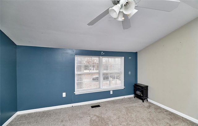 spare room featuring baseboards, carpet floors, a ceiling fan, and a wood stove