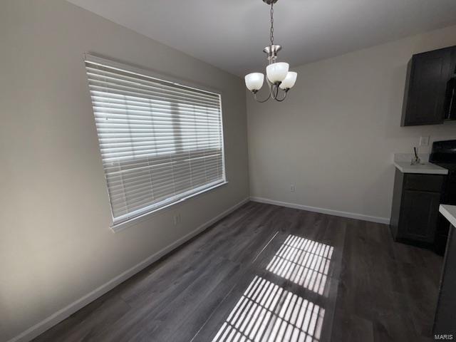 unfurnished dining area with dark wood-style floors, baseboards, and a chandelier