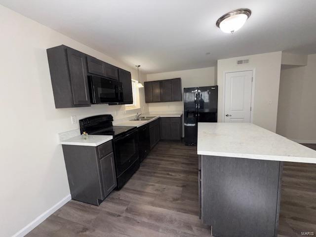 kitchen with visible vents, a kitchen island, light countertops, black appliances, and a sink