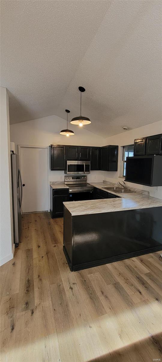 kitchen with dark cabinetry, lofted ceiling, stainless steel appliances, light countertops, and light wood-type flooring