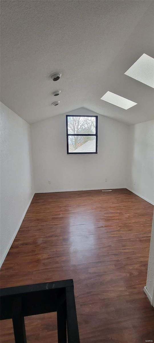 spare room featuring lofted ceiling with skylight, wood finished floors, and a textured ceiling