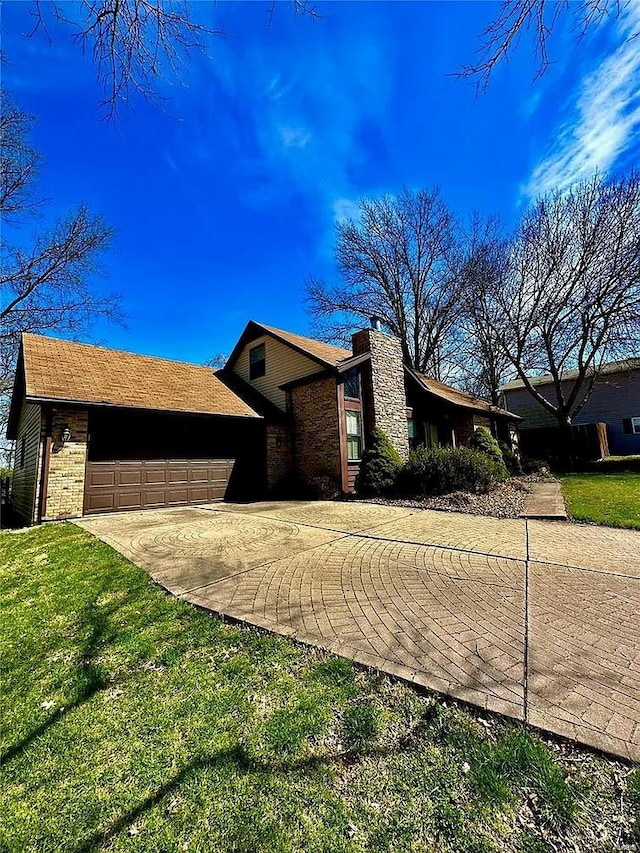 view of front facade with brick siding, a front lawn, concrete driveway, a chimney, and a garage