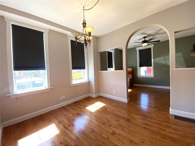 empty room with ceiling fan with notable chandelier, visible vents, wood finished floors, and baseboards