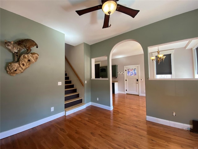 spare room featuring stairway, baseboards, wood finished floors, and ceiling fan with notable chandelier