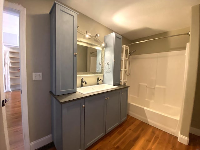 full bathroom with baseboards, vanity, wood finished floors, and washtub / shower combination