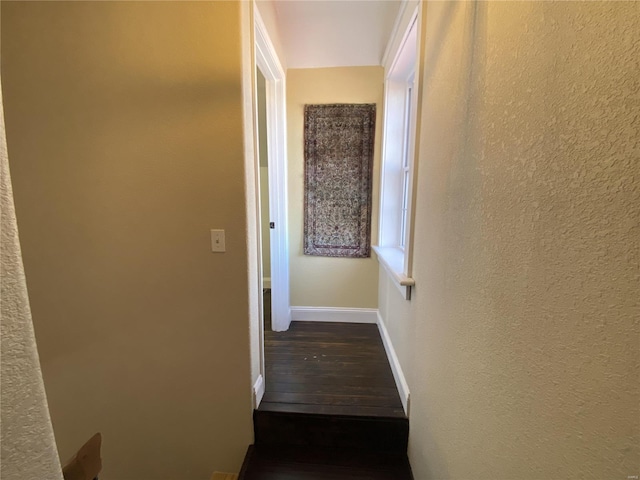 hallway featuring baseboards, dark wood-type flooring, and a textured wall