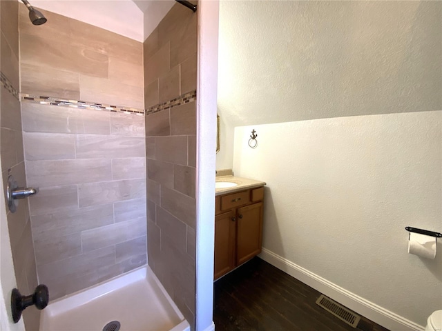 bathroom with visible vents, baseboards, tiled shower, wood finished floors, and vanity