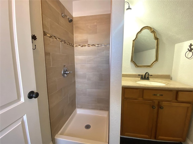 full bath featuring a textured wall, vanity, and a tile shower