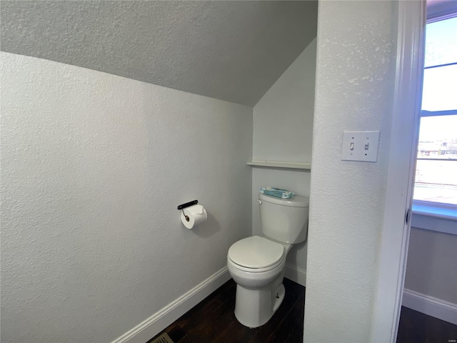 bathroom with wood finished floors, baseboards, lofted ceiling, toilet, and a textured wall