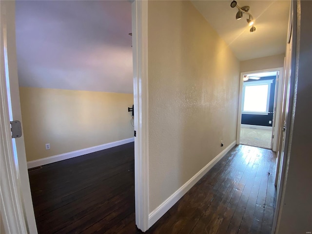 hall with track lighting, dark wood-type flooring, baseboards, and vaulted ceiling