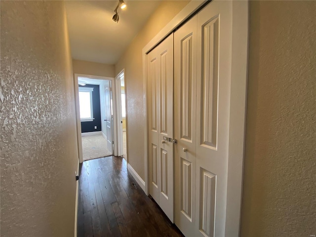 corridor featuring baseboards, dark wood finished floors, and a textured wall