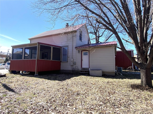 rear view of property featuring a chimney, metal roof, and a sunroom