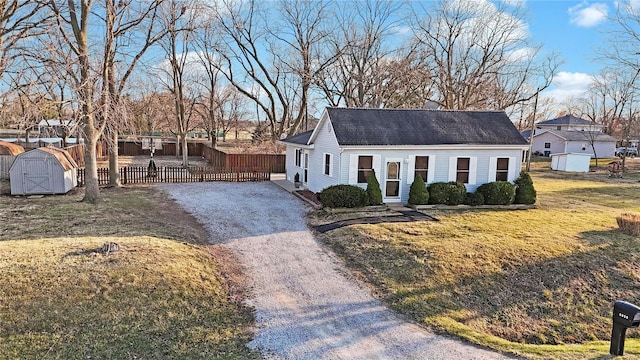 view of front of house with a front lawn, fence, a storage shed, an outbuilding, and driveway