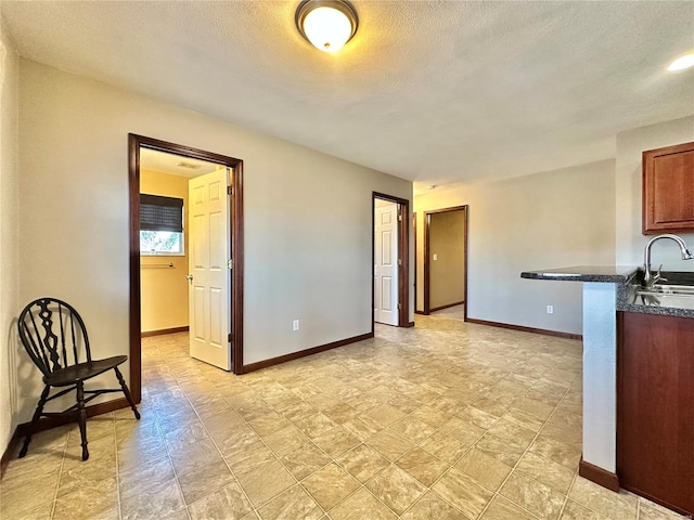 kitchen with a sink, baseboards, dark countertops, and a textured ceiling