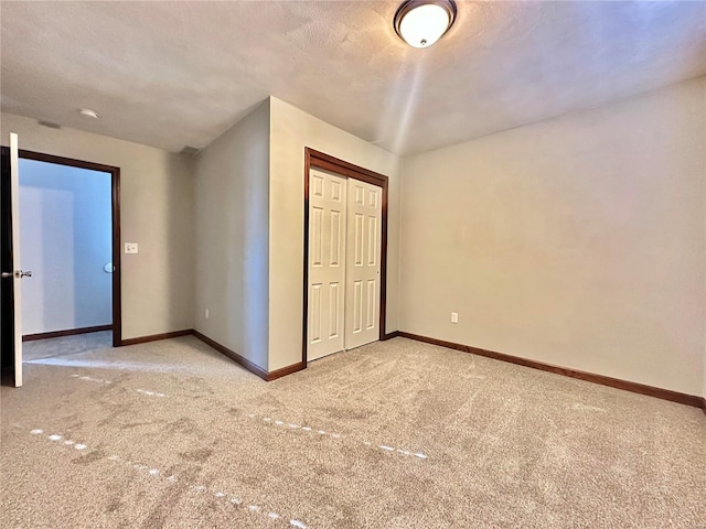 unfurnished bedroom with light colored carpet, baseboards, a closet, and a textured ceiling