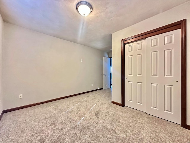 unfurnished bedroom featuring a closet, baseboards, a textured ceiling, and light carpet