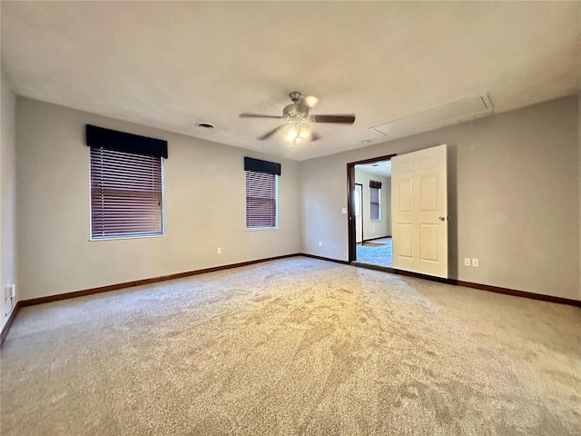 carpeted spare room featuring ceiling fan, attic access, and baseboards