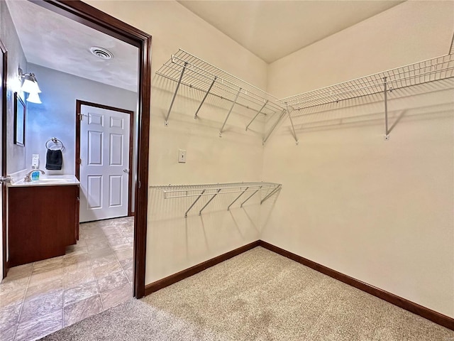 spacious closet with visible vents, light colored carpet, and a sink