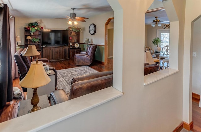 living area with a ceiling fan, wood finished floors, arched walkways, and baseboards