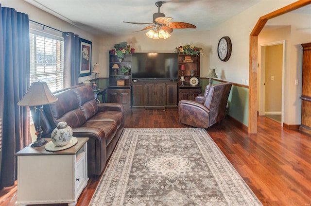 living room featuring arched walkways, baseboards, dark wood-type flooring, and ceiling fan