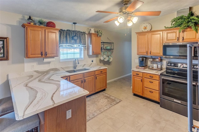 kitchen featuring light stone countertops, a peninsula, a sink, appliances with stainless steel finishes, and a kitchen breakfast bar