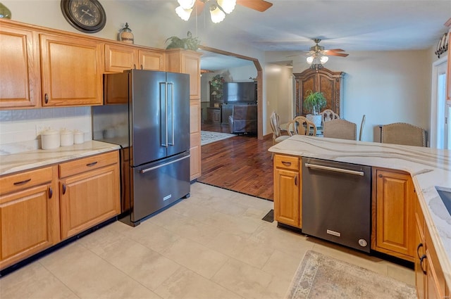 kitchen featuring stainless steel appliances, light stone countertops, decorative backsplash, and a ceiling fan