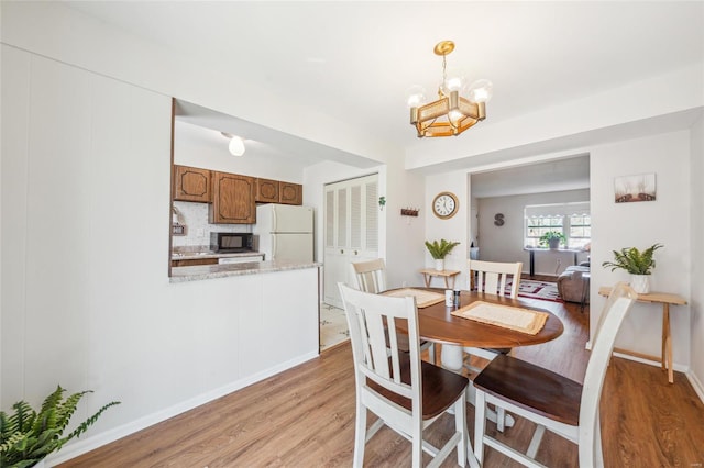 dining space with an inviting chandelier, baseboards, and light wood-type flooring